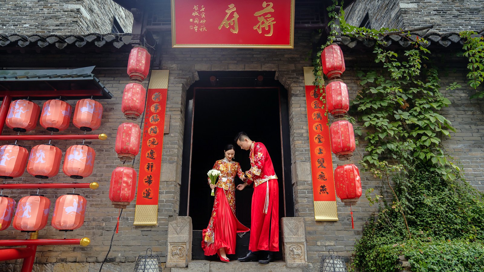 新人着秀禾服在徐州宅院门前相视，红灯笼映出中式喜气，枪花影像