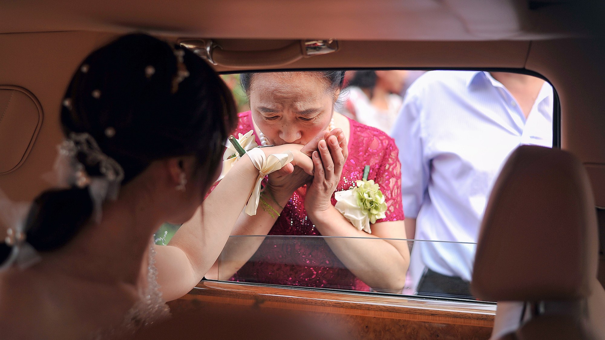 车窗边新娘与母亲轻吻道别，暖光映着红裙与胸花，沛县婚礼跟拍